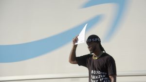 A story participant in UNION shades their eyes with a sheaf in paper , in front of a large Amazon sign